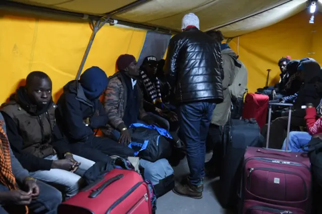 Migrants waiting to leave the Calais 'Jungle' camp with suitcases