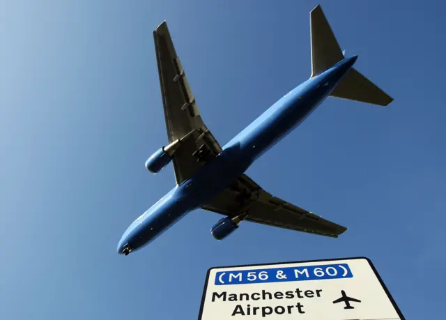 Plane flying over road sign showing the way to Manchester airport