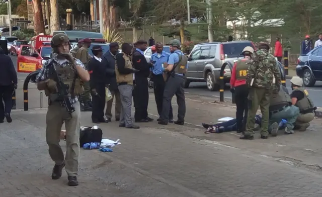 Unidentified U.S. Embassy personnel and Kenyan security forces stand near to the body, right, of a man who was killed outside the U.S. Embassy in Nairobi, Kenya Thursday, Oct. 27, 2016