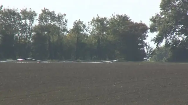 Taped-off area in the field, in front of woodland