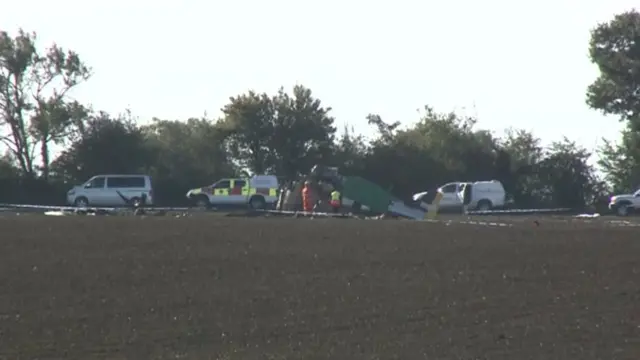 Vehicles and people in fluorescent clothing by the wreckage of the plane