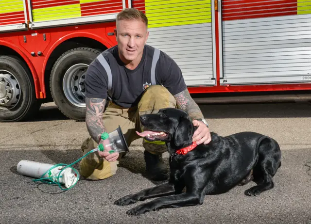 Firefighter and black labrador dog demonstrate the new pet oxygen masks