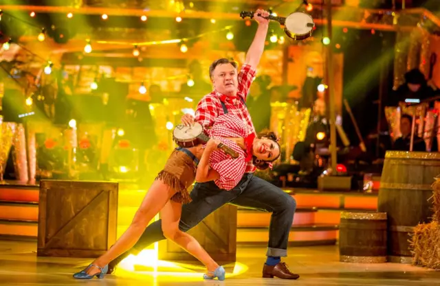 Ed Balls in check shirt, holding banjo, with dancer Katya Jones