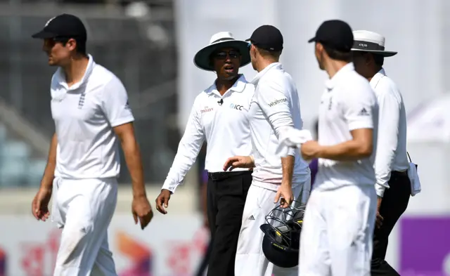 The match umpires talk to Joe Root