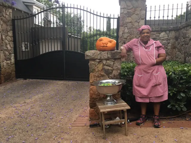 Woman stands next to pumpkin with platter of sweets on a small table