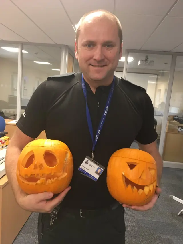 Police officer holding two carved pumpkins