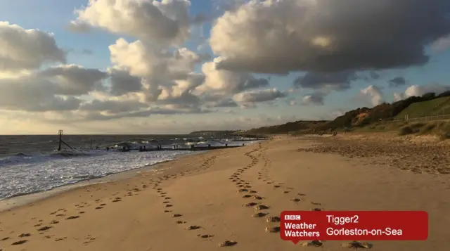Footprints on a sandy beach, with clouds in the sky