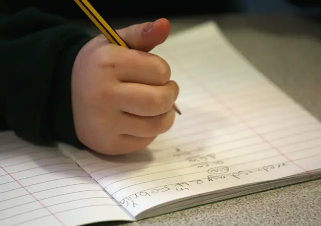 A child holding a pencil in the right hand, with a school exercise book