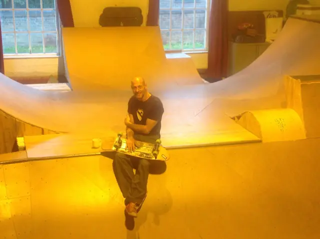 Rob Marsden, with skateboard, sitting in his skate bowl