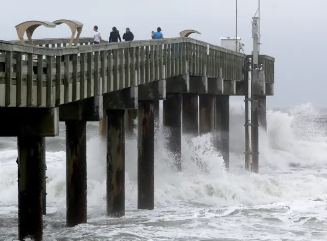 People stand on the pier as waves crash below as Hurricane Matthew approaches on Thursday, Oct. 6, 2016 in St. Augustine, Fla