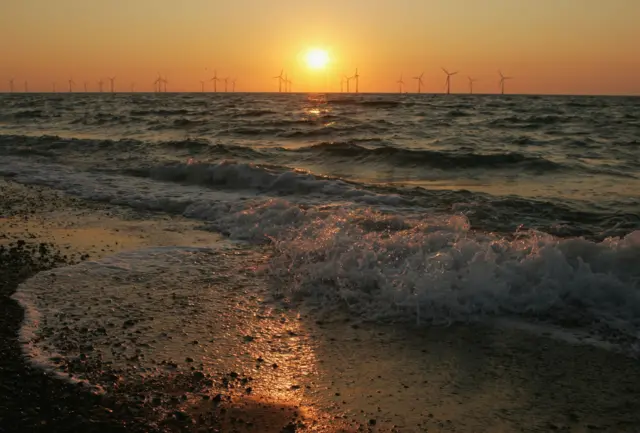 The sun rising behind a North Sea offshore wind farm