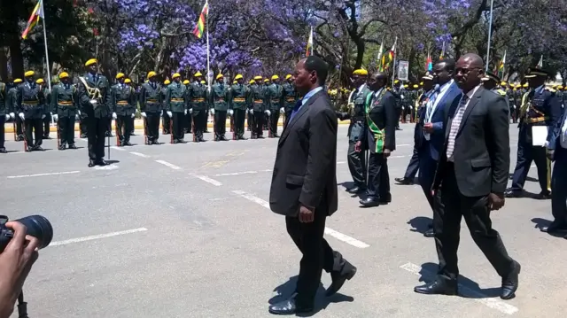 Robert Mugabe proceeds past guards wearing bright yellow berets