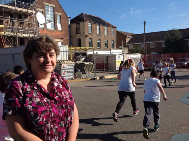 Headteacher Melodie Fearns in pink patterned top, in the school playground, with children in the backgroudn