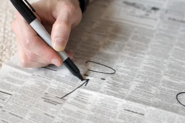 An unemployed person circling jobs in a newspaper.