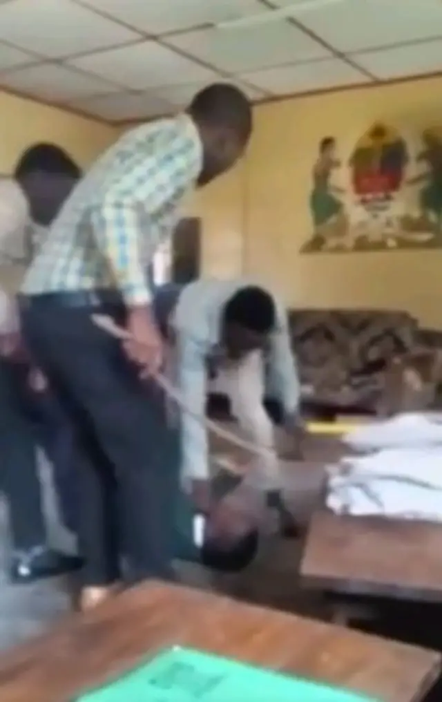 Men standing over boy - a screengrab from the video