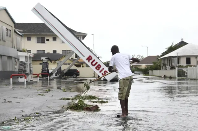 06/10/2016 Associated Press Marco Beckford rakes up debris from a storm drain as he begins the cleanup near a damaged petrol station in the aftermath of Hurricane Matthew in Nassau, Bahamas, Thursday, Oct. 6, 2016