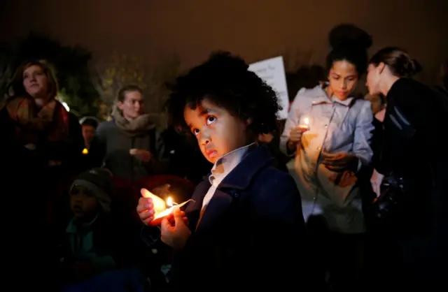 A young boy stands with other anti-Trump demonstrators during a candlelight vigil in front of the White House in Washington