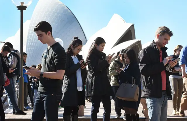 People on phones outside Sydney Opera House
