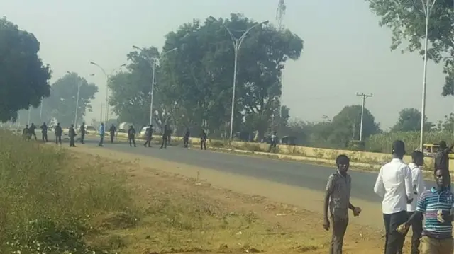 Young men pitctured in foreground with police lined up across the road