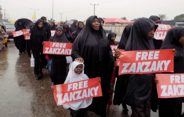 Women and young children carrying placards with "Free Zakzaky" walk down the road in Kano