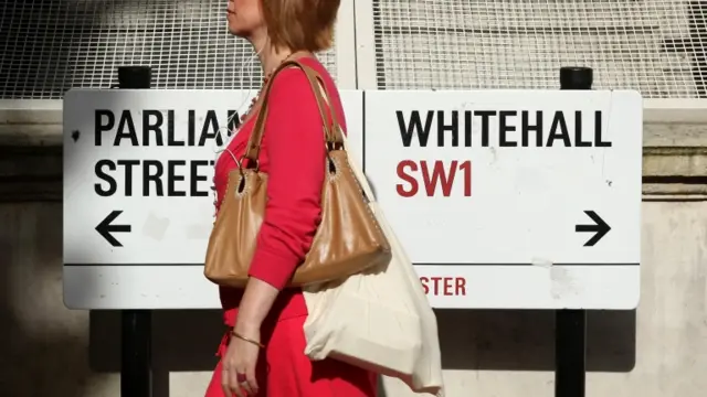 A pedestrian walking past a sign on Whitehall, London