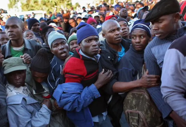 Immigrants watch as others jump the queue to apply for asylum as refugees at a government refugee center June 17, 2008 in Johannesburg, South Africa.