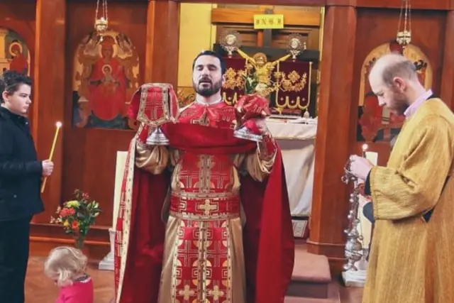 A priest in red and gold taking part in a Romanian Orthodox church service