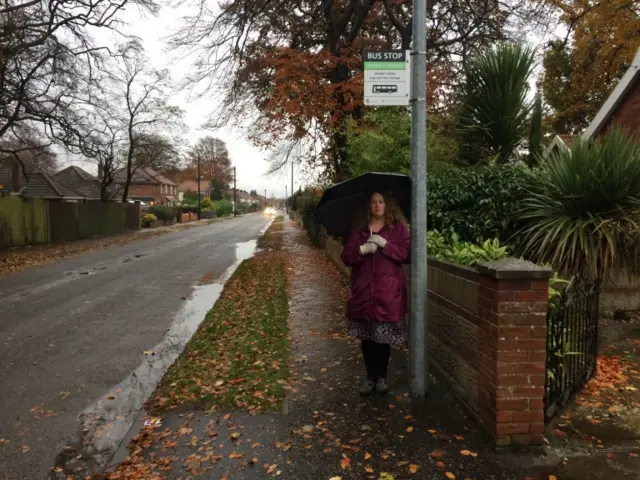 Natasha Harpley standing at bus stop, with umbrella