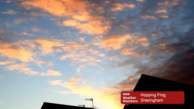 Sun-touched clouds in a light blue sky, with silhouettes of roof tops