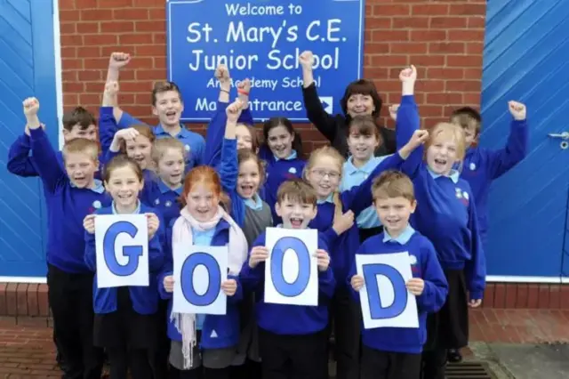 Pupils in blue uniform holding up letters spelling Good