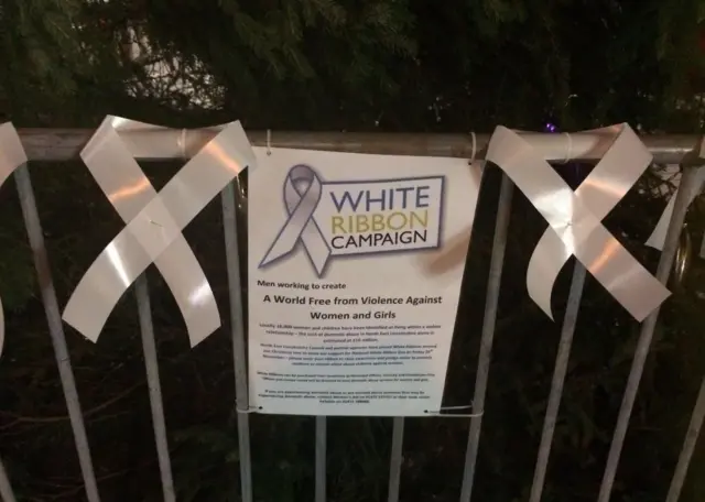 White ribbons and sign in front of a Christmas tree