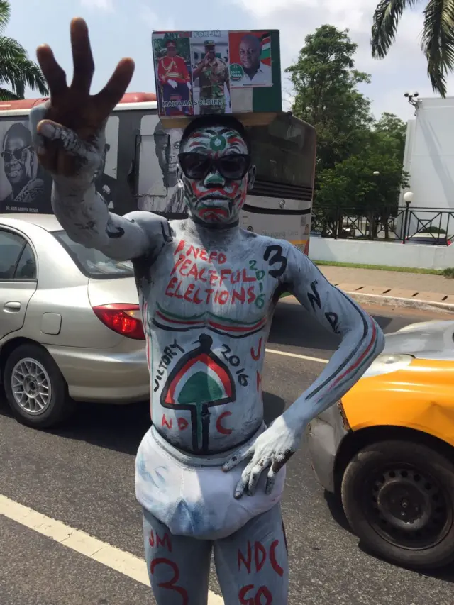 Man in facepaint and bodypaint with messages like "I need peaceful elections" and " victory 2016" written on him