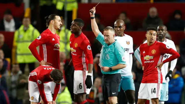 Paul Pogba is booked by referee Jonathan Moss