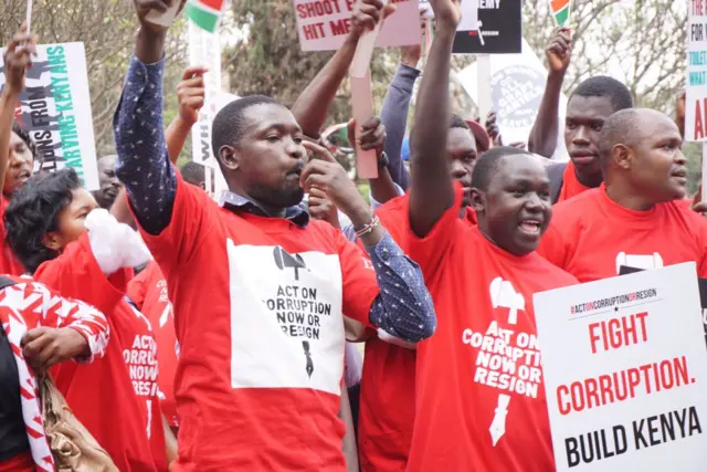 Protesters with red t-shirts and placards saying things like "Fight Corruption. Build Kenya"