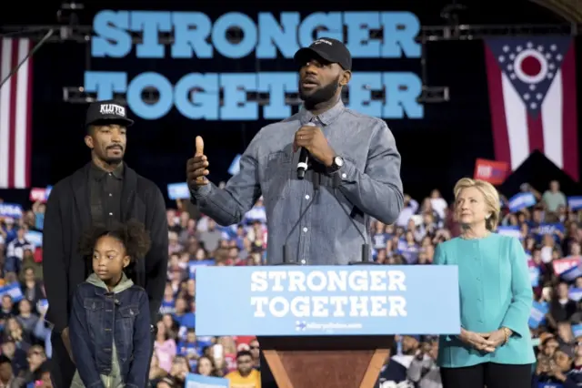 LeBron James, center, accompanied by Cleveland Cavaliers basketball player J. R. Smith, left, his daughter Demi, bottom left, and Democratic presidential candidate Hillary Clinton, right, speaks at a rally at the Cleveland Public Auditorium in Cleveland, Sunday, Nov. 6, 2016