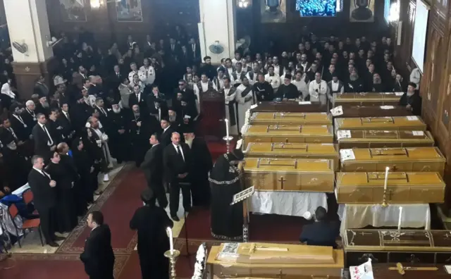 Egyptians and clergymen stand next to the coffins of the victims of a bomb explosion that targeted a Coptic Orthodox Church the previous day in Cairo, during their funeral in the Egyptian capital"s Nassr City neighbourhood on December 12, 2016.