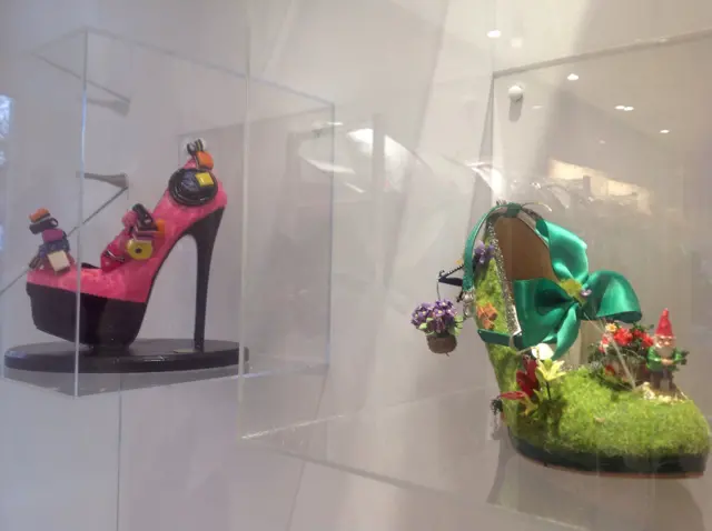 Pink high-heeled shoe with licquorice allsorts on them, and a green floral shoe, with moss and a gnome