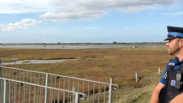 Police officer, standing on right, looking over Breydon Water