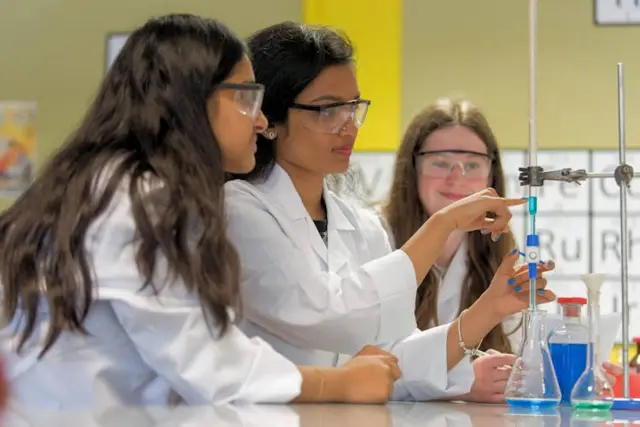 Three girl students at Notre Dame High School, in a science laboratory, wearing white coats and protective glasses