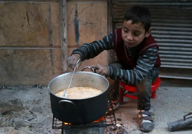 A child cooks food in a street in rebel-held Aleppo (13 December 2016)