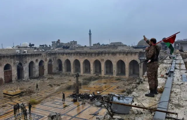 Member of pro-government forces holds flag on top of roof of Aleppo's Great Mosque in Aleppo (13 December 2016)