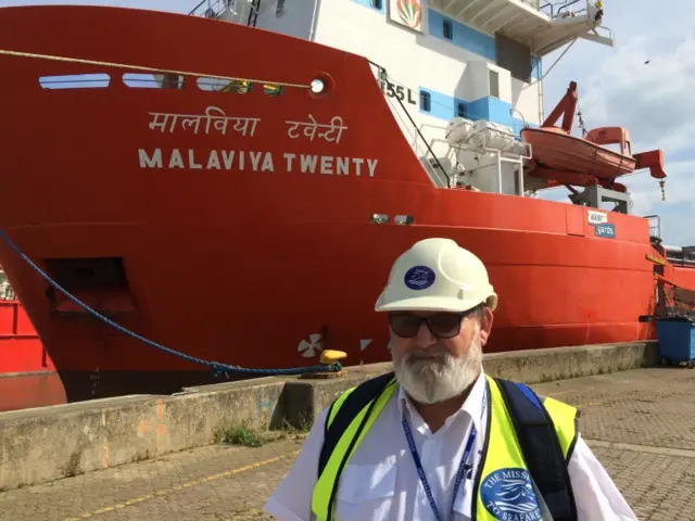 Revd Peter Paine, in hard hat and reflective jacket, standing by the Malviya Twenty