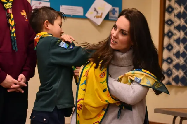 Dylan putting a yellow scarf around the arm of the Duchess of Cambridge