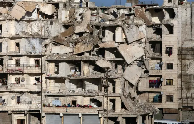 Residents in a government-held part of Aleppo"s Salaheddin neighbourhood watch from their damaged homes as buses evacuate rebel fighters and their families from rebel-held neighbourhoods in Aleppo