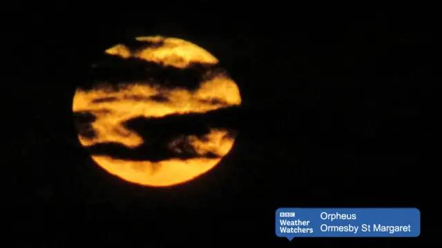 A golden moon with bands of cloud, in a dark sky