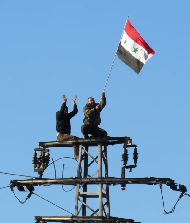 Syrian pro-government forces wave their national flag during an evacuation operation of rebel fighters and their families from rebel-held neighbourhoods in the embattled city of Aleppo