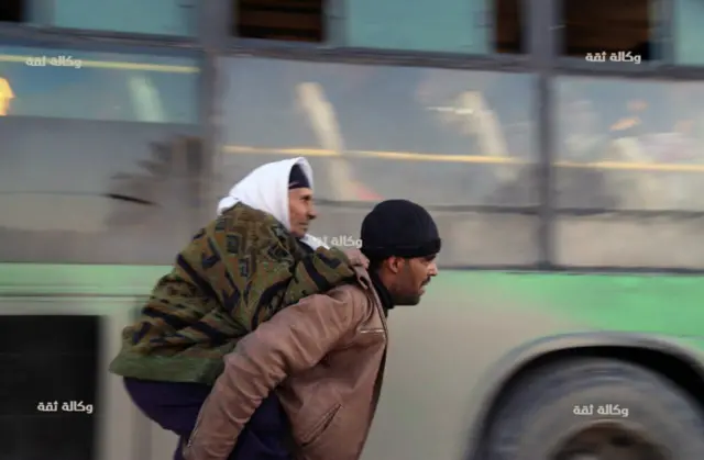 A Syrian man carrying an elderly woman to a bus for evacuation from eastern Aleppo