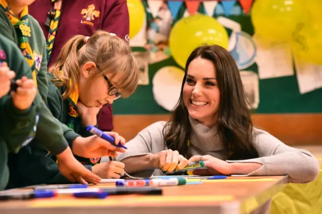 The Duchess of Cambridge crouching at a table with girl Cub Scouts drawing