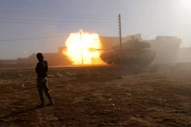 A rebel fighter stands near a Turkish tank as it fires towards Guzhe village, northern Aleppo