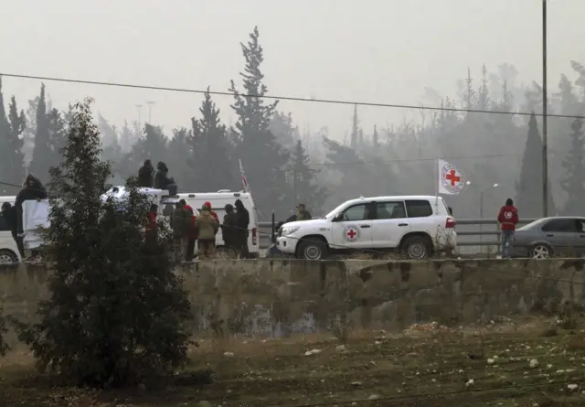 In this photo released by the Syrian official news agency SANA, civilians gather near the Red Cross vehicles for evacuation from eastern Aleppo, Syria, Friday, Dec. 16, 2016.